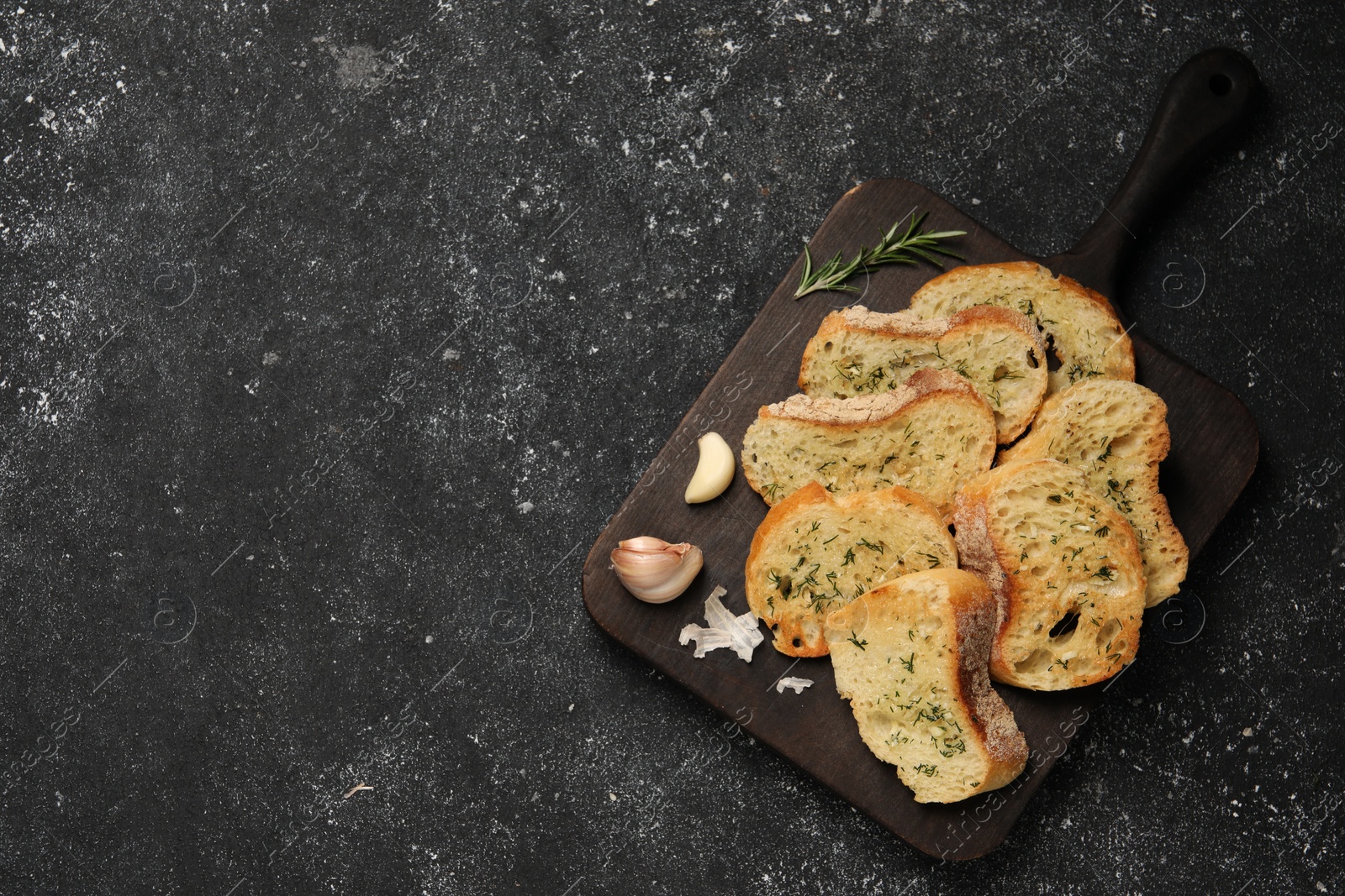 Photo of Tasty baguette with garlic, dill and rosemary on grey textured table, top view. Space for text
