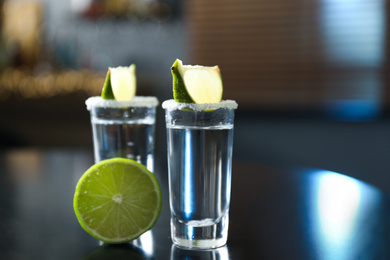 Photo of Mexican Tequila with salt and lime slices on black table at bar
