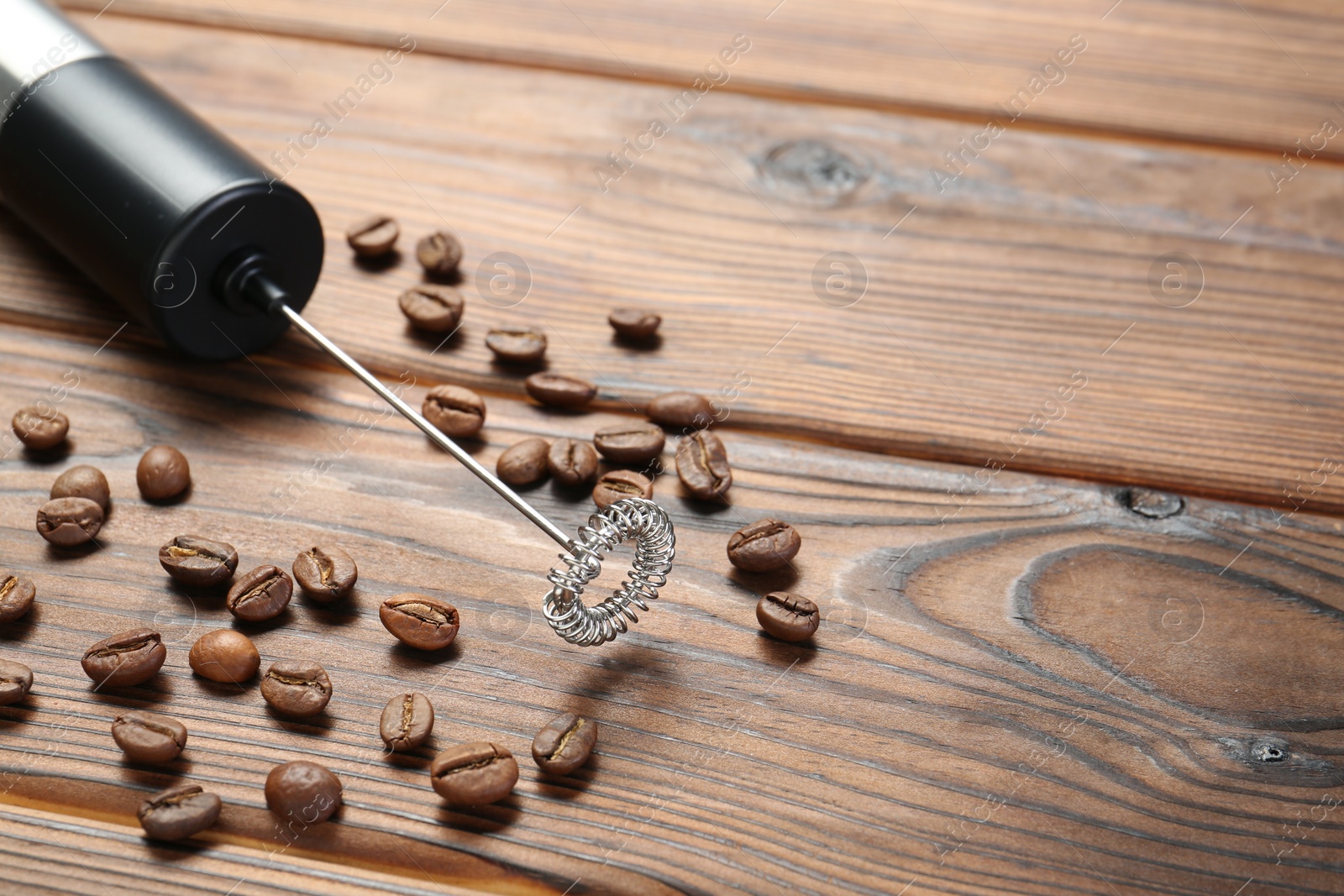 Photo of Black milk frother wand and coffee beans on wooden table, closeup. Space for text