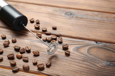 Photo of Black milk frother wand and coffee beans on wooden table, closeup. Space for text