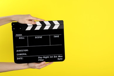 Photo of Woman holding movie clapper on yellow background, closeup. Space for text