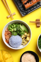 Photo of Delicious sushi rolls and poke bowls on yellow background, flat lay
