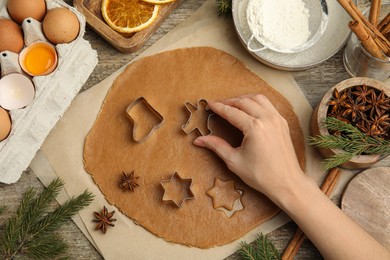 Photo of Woman cutting dough with cookie cutter at wooden table, top view. Christmas biscuits