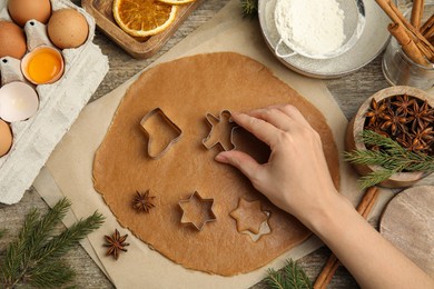 Woman cutting dough with cookie cutter at wooden table, top view. Christmas biscuits