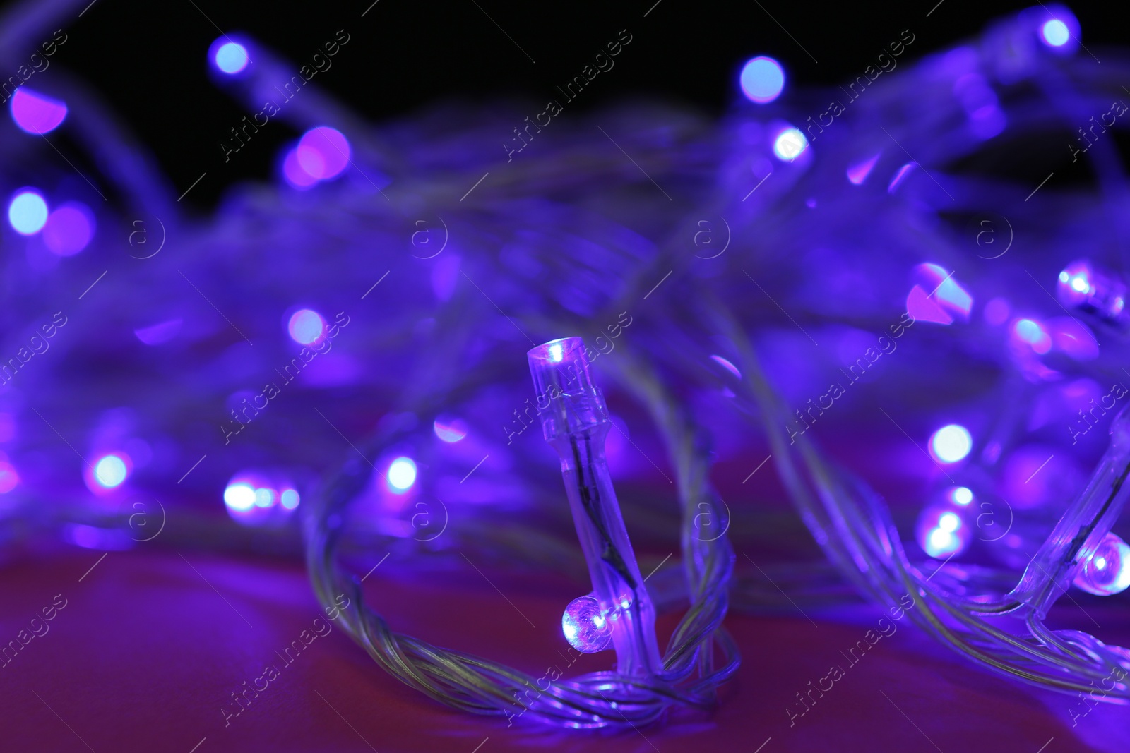 Photo of Glowing Christmas lights on burgundy background, closeup