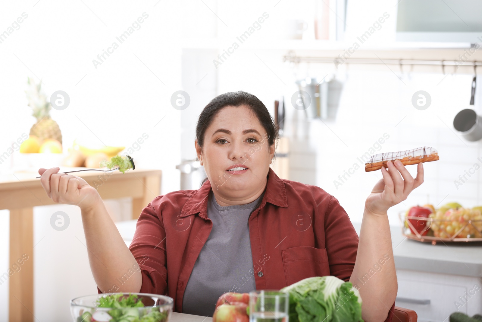 Photo of Woman choosing between vegetable salad and dessert in kitchen. Healthy diet