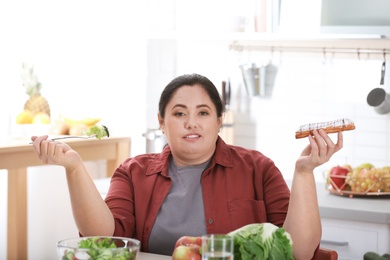 Woman choosing between vegetable salad and dessert in kitchen. Healthy diet