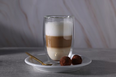 Photo of Aromatic latte macchiato in glass and chocolate candies on grey table