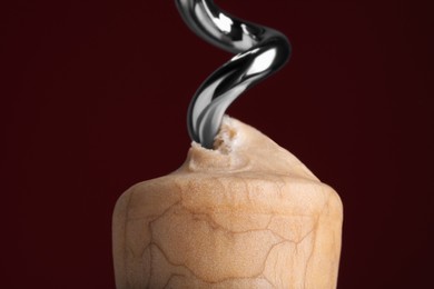 Photo of Corkscrew and wine cork on burgundy background, closeup
