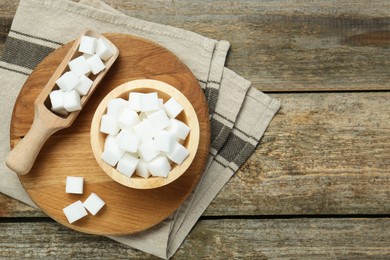 White sugar cubes in bowl and scoop on wooden table, top view. Space for text