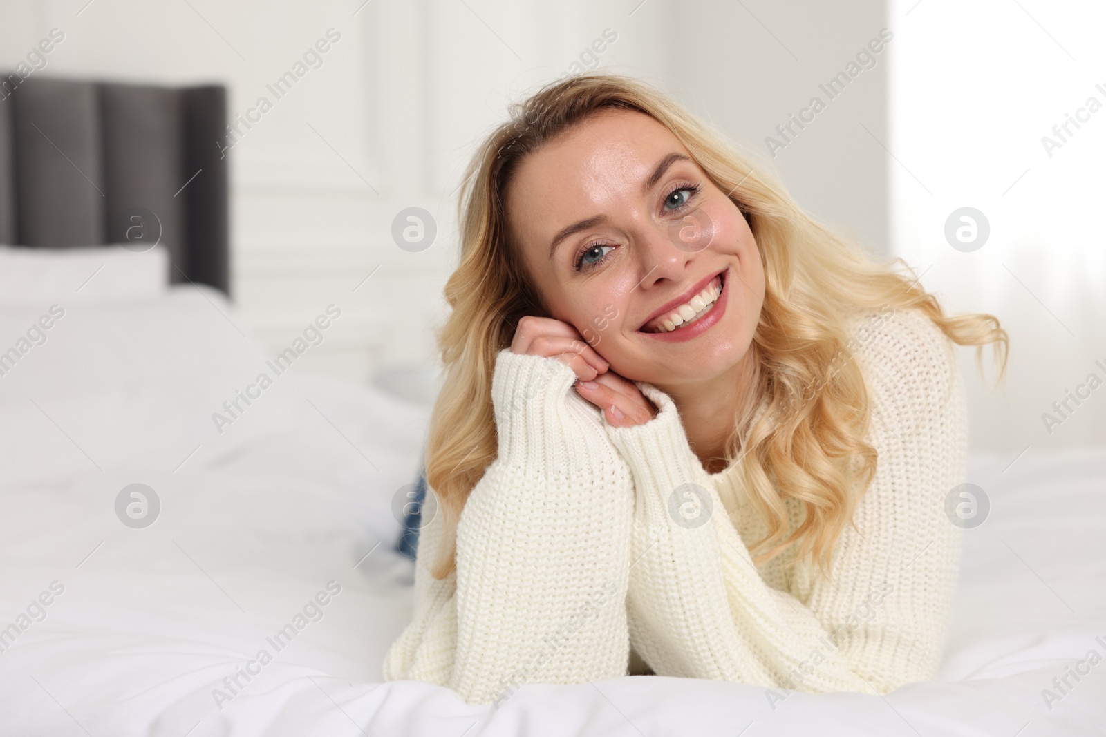 Photo of Happy woman in stylish warm sweater lying on bed indoors. Space for text