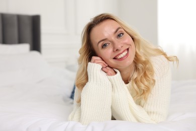 Photo of Happy woman in stylish warm sweater lying on bed indoors. Space for text