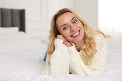 Happy woman in stylish warm sweater lying on bed indoors. Space for text