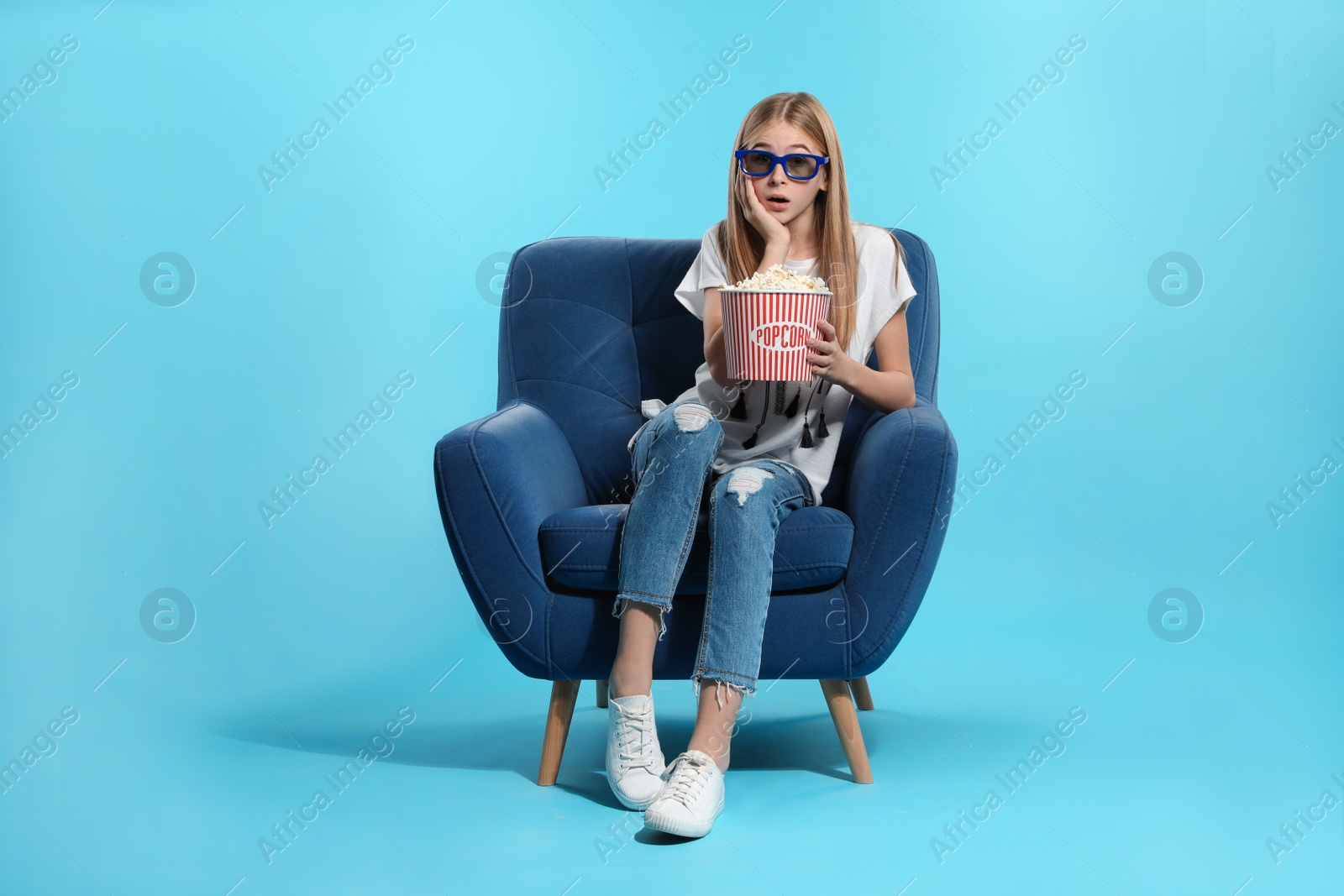 Photo of Emotional teenage girl with 3D glasses and popcorn sitting in armchair during cinema show on color background