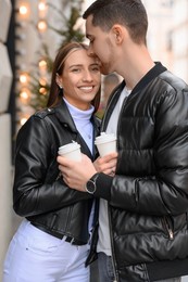 Photo of Lovely young couple with cups of coffee enjoying time together outdoors, closeup. Romantic date