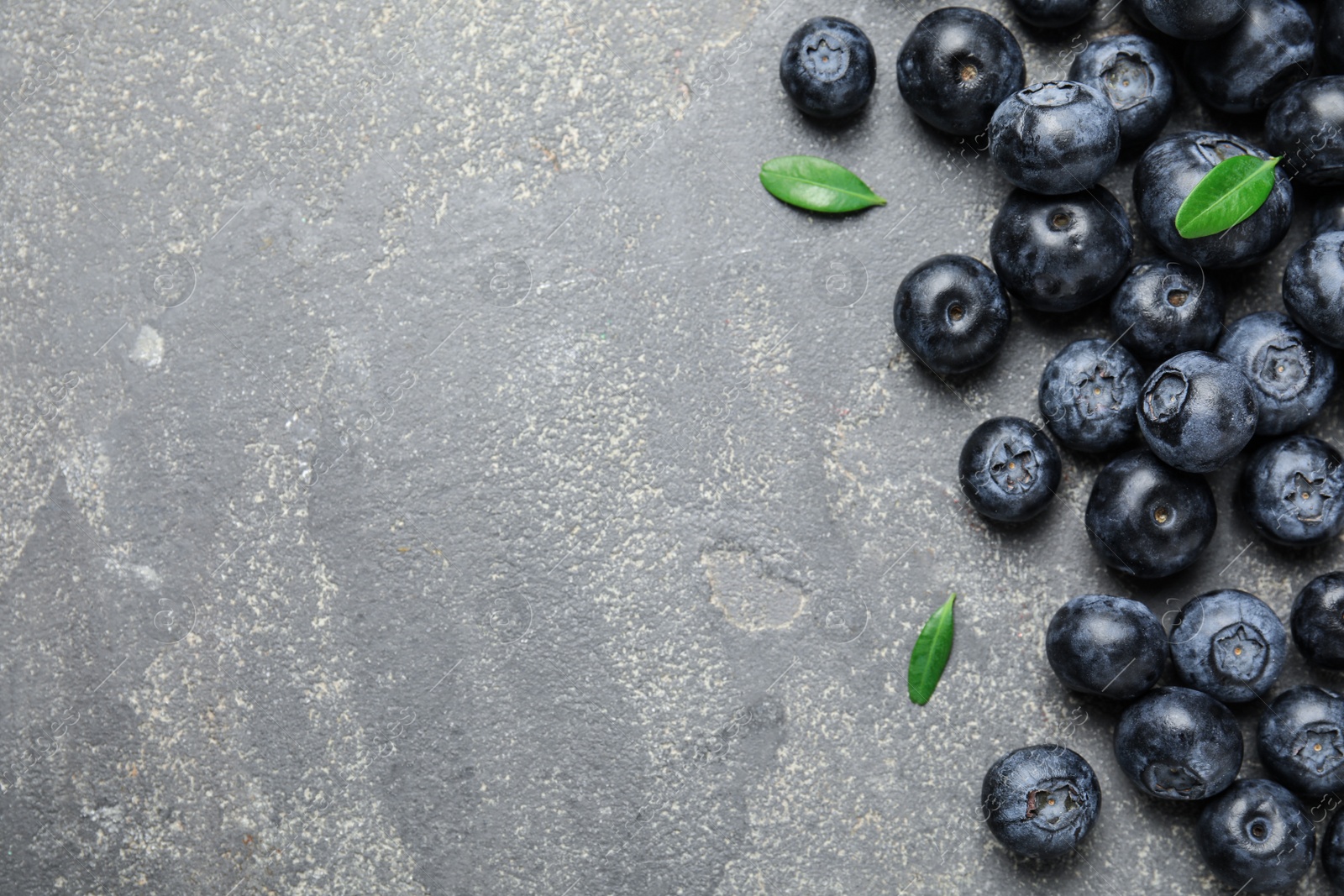 Photo of Tasty fresh blueberries and leaves on grey stone background, top view with space for text