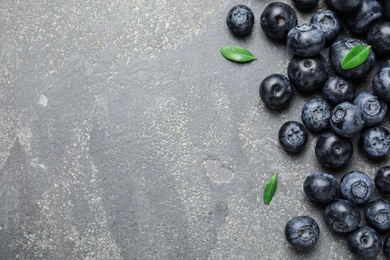 Photo of Tasty fresh blueberries and leaves on grey stone background, top view with space for text