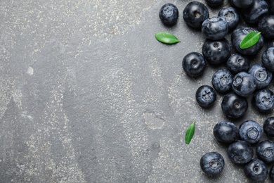 Tasty fresh blueberries and leaves on grey stone background, top view with space for text