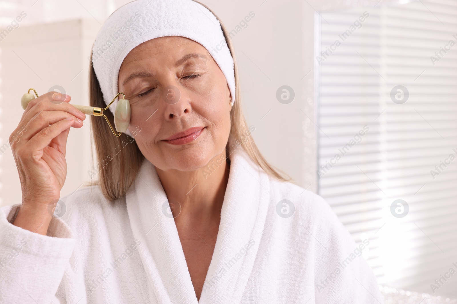 Photo of Woman massaging her face with jade roller in bathroom. Space for text