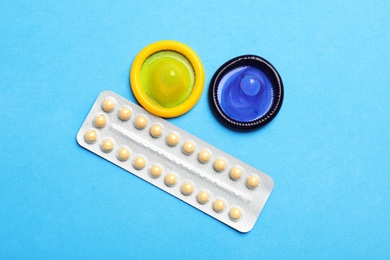 Photo of Condoms and birth control pills on light blue background, flat lay. Safe sex concept