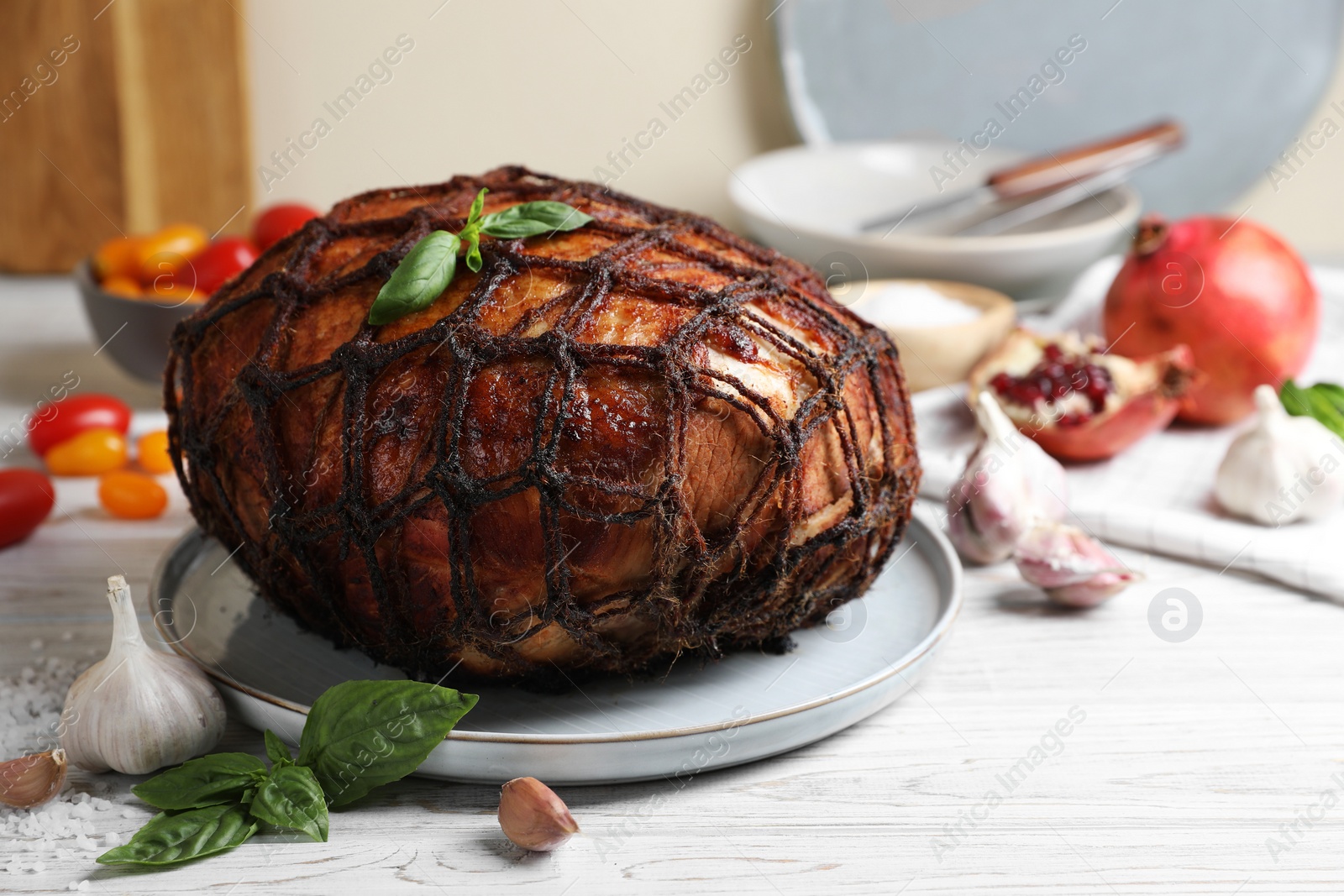 Photo of Delicious baked ham, basil leaves and garlic on white wooden table