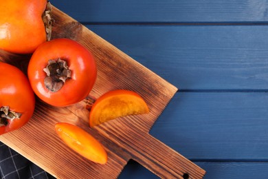 Photo of Delicious ripe persimmons on blue wooden table, top view. Space for text