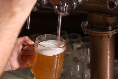 Photo of Bartender pouring beer from tap into glass in bar, closeup