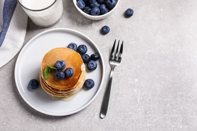 Plate of tasty pancakes with blueberries and honey on light grey table, flat lay. Space for text