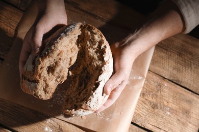 Photo of Man breaking loaf of fresh bread at wooden table, top view