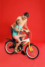 Photo of Young mother teaching daughter to ride bicycle on red background