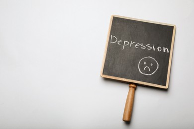 Photo of Chalkboard with word Depression and drawing of sad face on white background, top view. Space for text