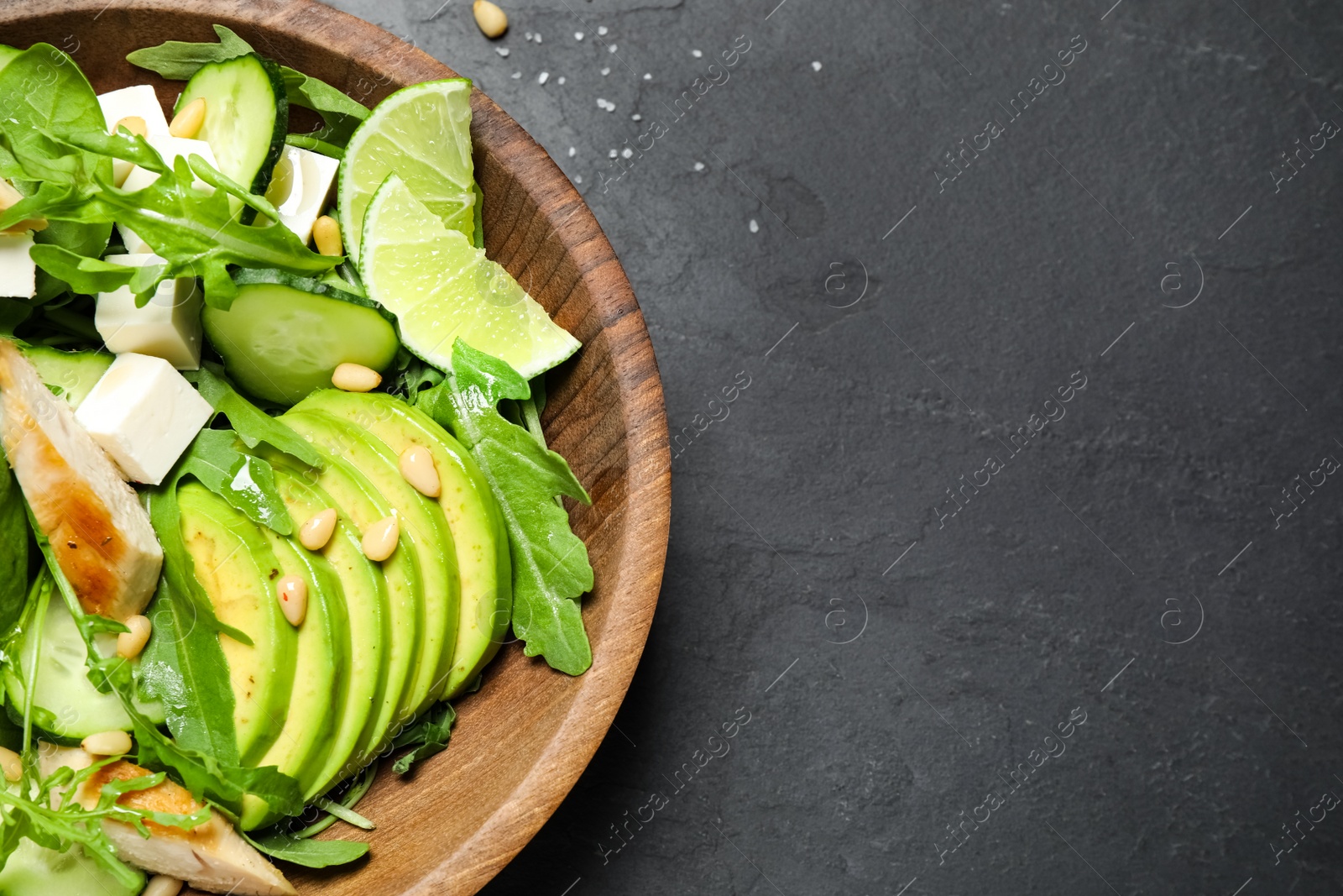 Photo of Delicious salad with chicken, arugula and avocado on black table, above view. Space for text