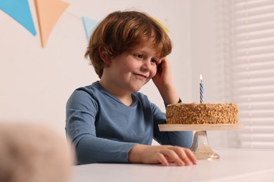 Cute boy with birthday cake at white table indoors