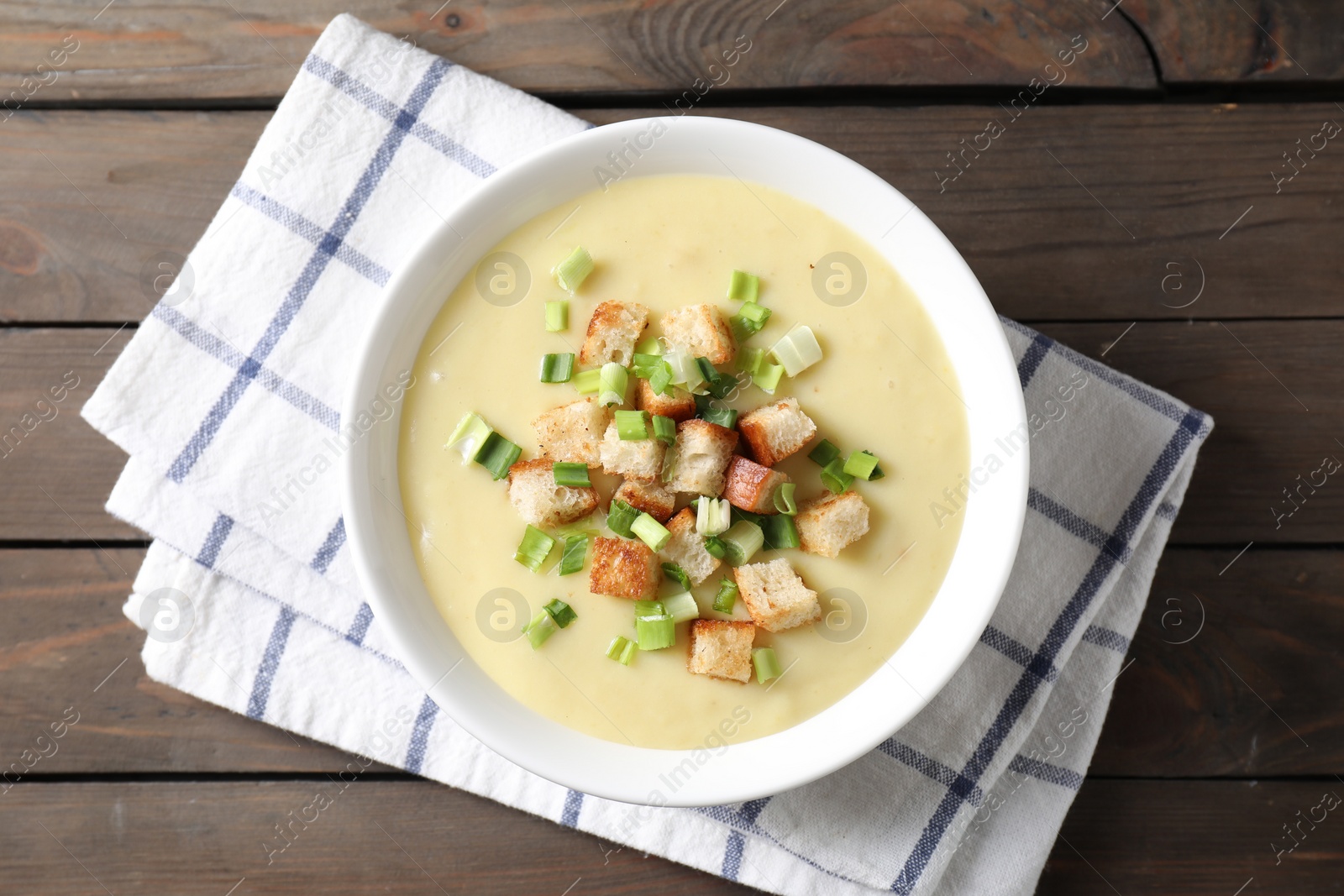 Photo of Tasty potato soup with croutons and green onion in bowl on wooden table, top view