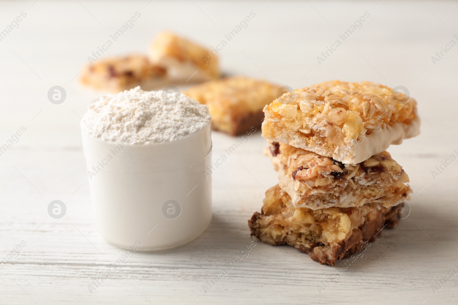 Photo of Tasty protein bars and scoop of powder on white table