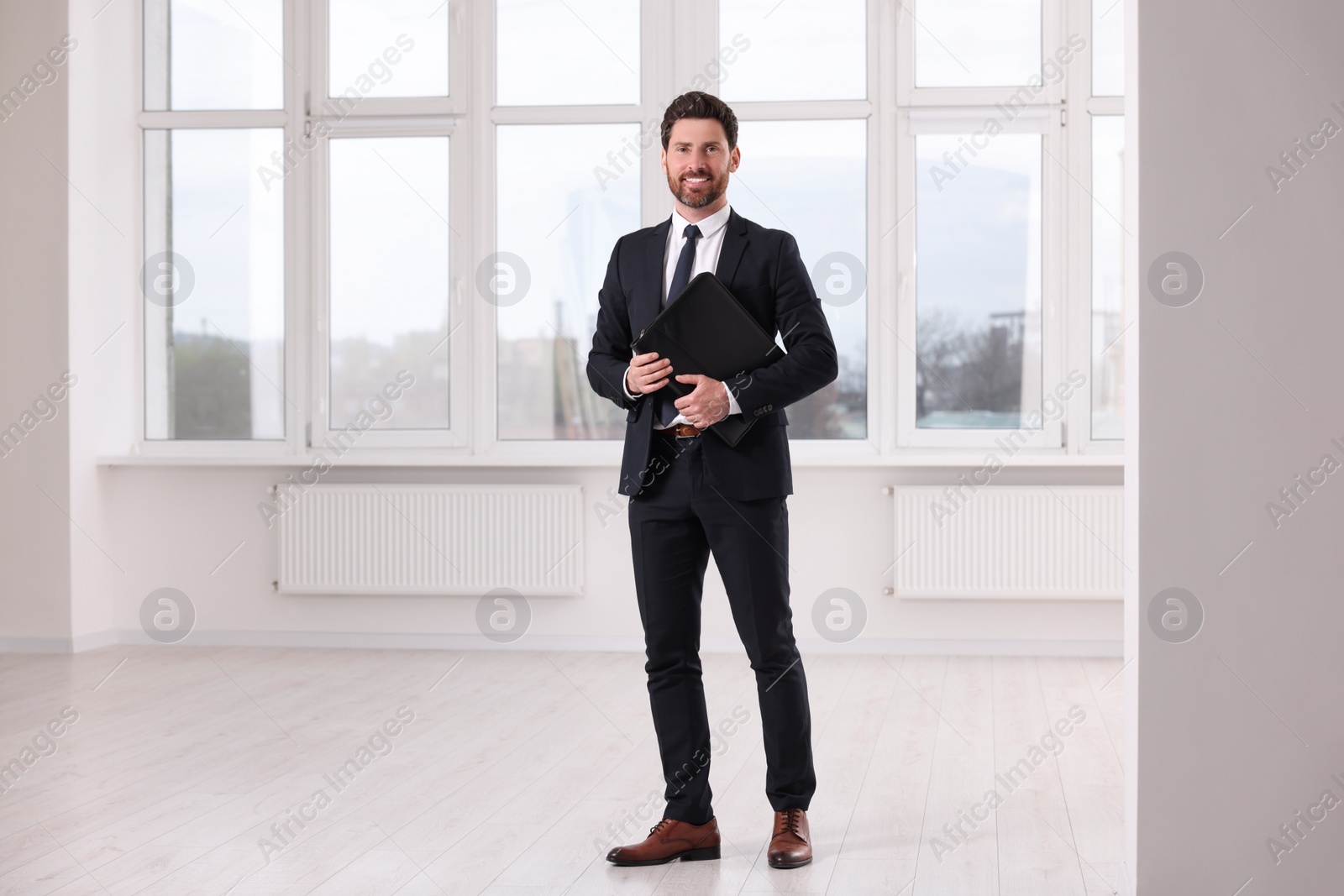 Photo of Happy real estate agent with leather portfolio in new apartment