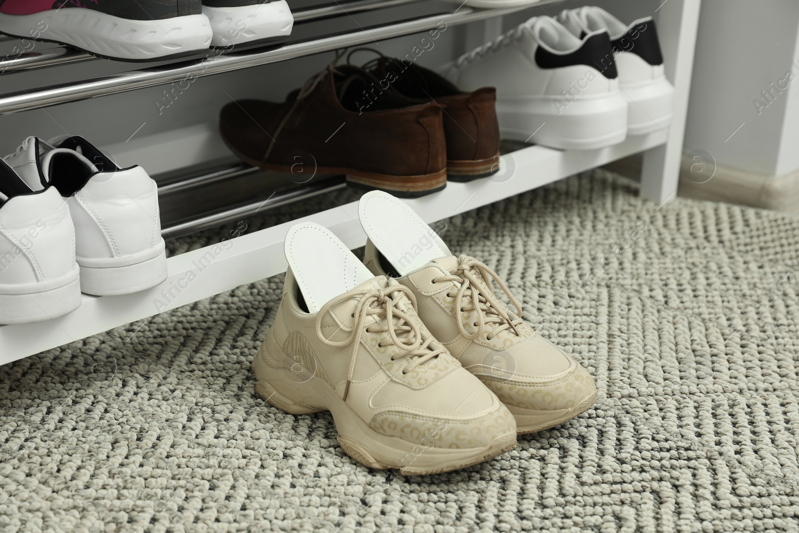 Photo of Orthopedic insoles in shoes on rug near rack, closeup