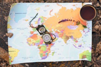 Photo of Compass, mug with drink and map on rock outdoors, top view. Camping season