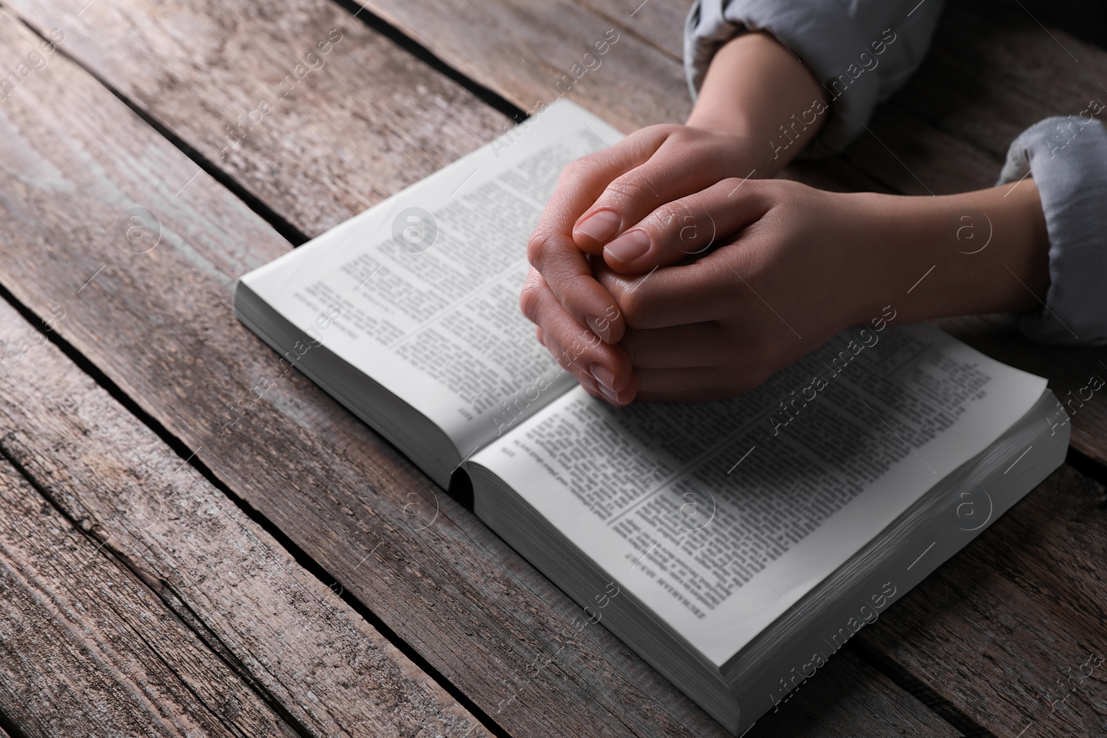 Photo of Religion. Christian woman praying over Bible at wooden table, closeup