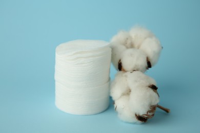 Photo of Stack of cotton pads and flowers on light blue background, closeup