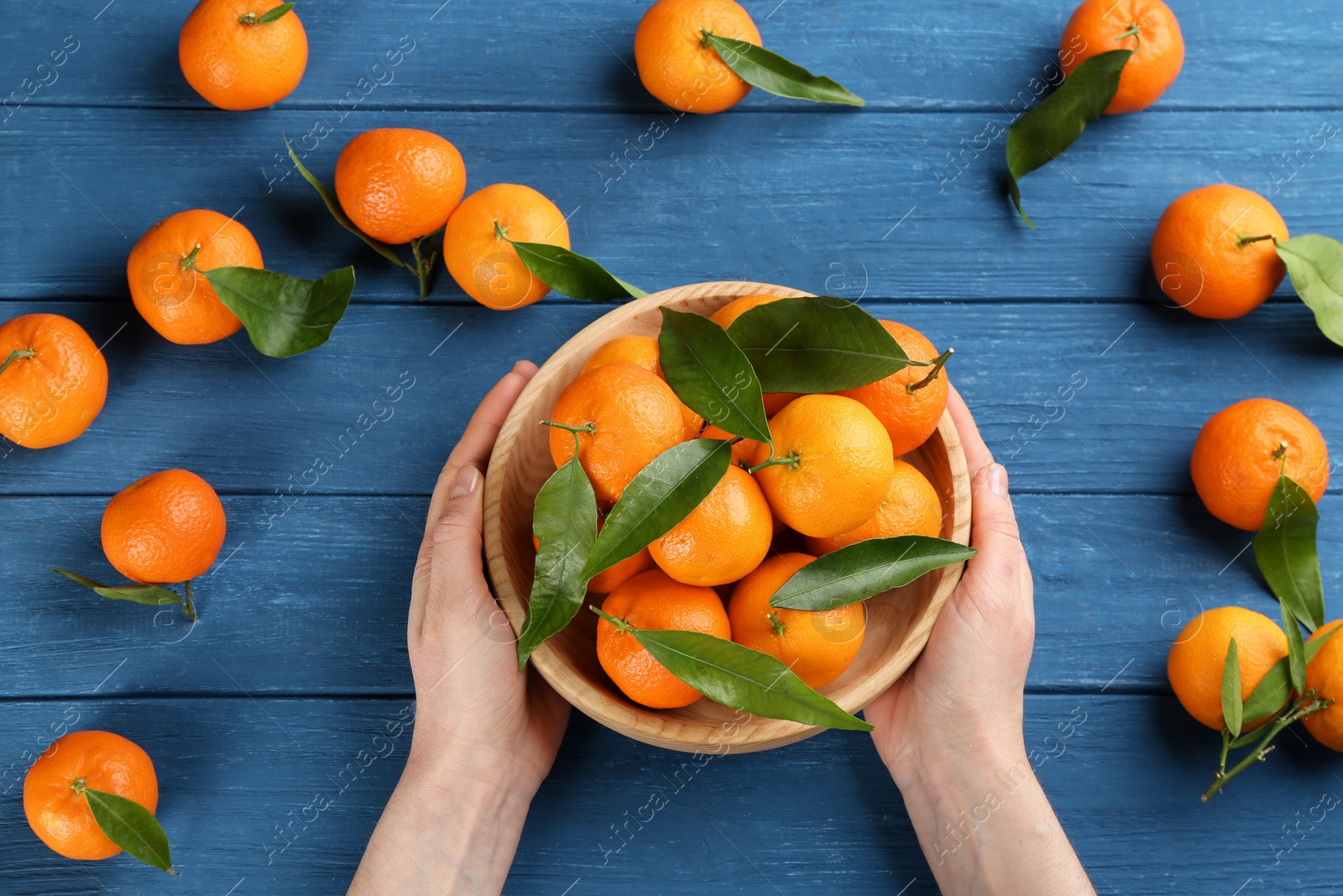 Photo of Woman with fresh ripe tangerines at blue wooden table, top view