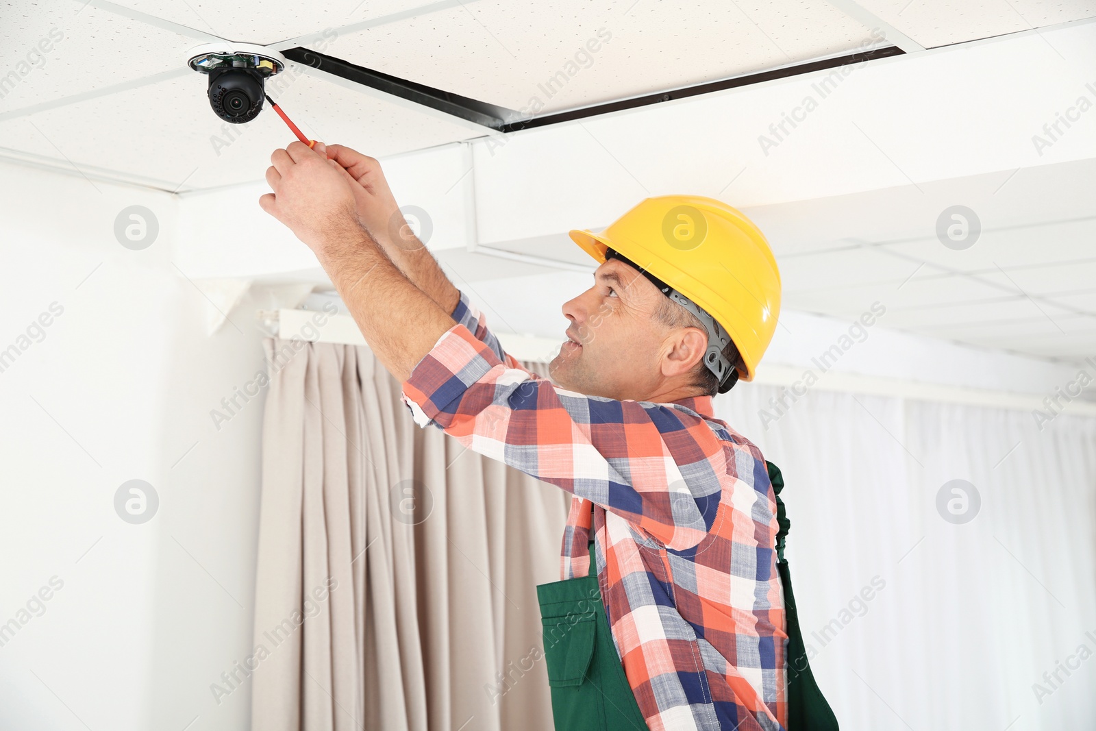 Photo of Electrician with screwdriver repairing CCTV camera indoors