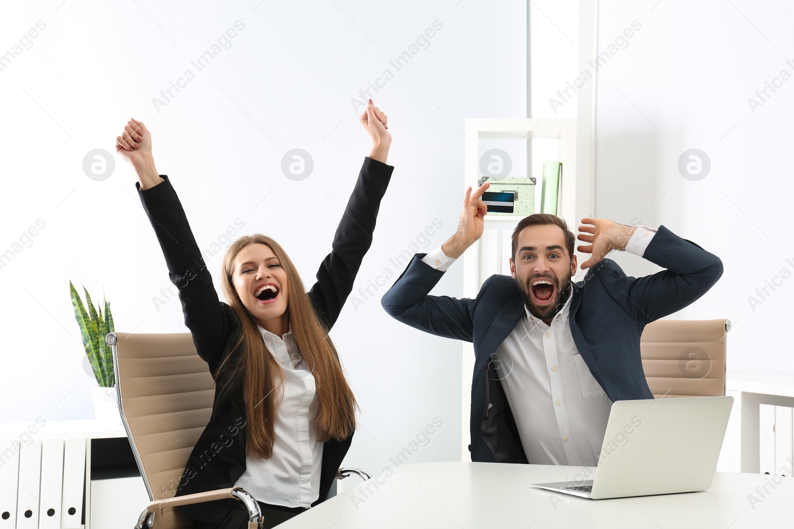 Photo of Emotional young people with credit card and laptop celebrating victory in office