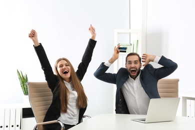 Emotional young people with credit card and laptop celebrating victory in office
