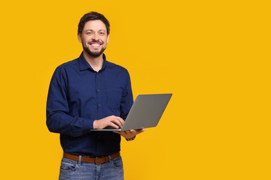 Photo of Happy man with laptop on yellow background, space for text