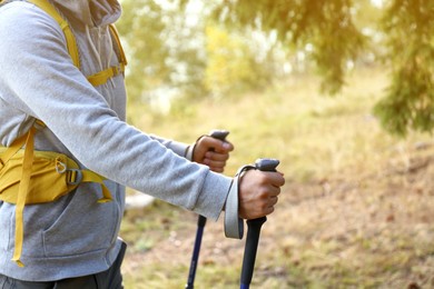 Photo of Man with backpack and trekking poles hiking in forest, closeup
