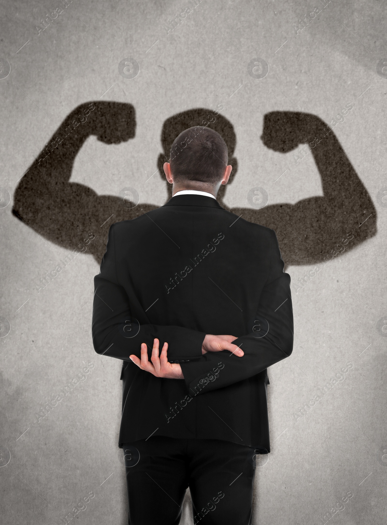 Image of Businessman and shadow of strong muscular man in front of him on grey wall. Concept of inner strength
