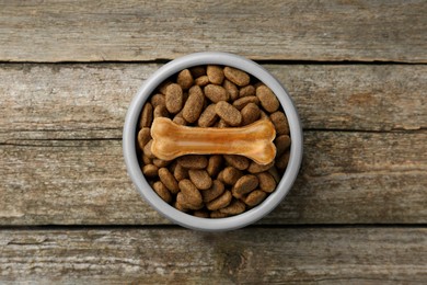 Photo of Dry dog food and treat (chew bone) on wooden floor, top view