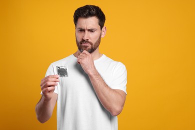 Photo of Confused man holding condom on yellow background. Safe sex