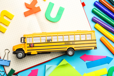 Photo of Flat lay composition with yellow school bus model on light blue background. Transport for students